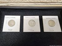 Photo showing 3 Buffalo nickels from 1927, 1928, and 1929 in white cardboard holders.