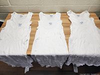 Six white Gildan men's sleeveless undershirts size XL laid out on table.