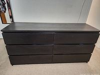 Front view of black dresser showing six drawers and flat top surface.