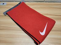 Full view of the folded red Nike golf towel with black edges on wood surface