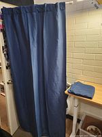 Navy blue Eclipse curtain panel hanging from a white curtain rod, covering a doorway. Another curtain panel folded on a wooden desk nearby.