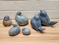 Front and side view of five bird figurines on a wooden surface against a brick wall, showing details and textures of each piece.