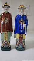 Photo showing both antique Chinese porcelain statues standing side by side against a light background.