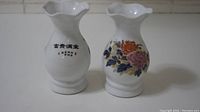 Photo showing front and back views of two Chinese white porcelain vases with floral decorations and Chinese characters.