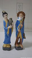 Full view of both Japanese porcelain figurines, woman and elderly man