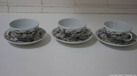 Three porcelain tea cups with matching saucers displayed side by side, showing detailed floral patterns.