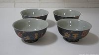 Four black speckled ceramic bowls with Japanese characters and floral designs, shown from above and side angle