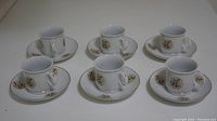 Six sets of cups and saucers arranged on a surface, showing floral patterns and gold trim.