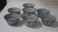 Seven antique small Chinese porcelain bowls with blue and white hand-painted designs, arranged in two rows on white surface.
