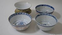 Four antique Chinese porcelain pieces including three bowls and one cup on white surface