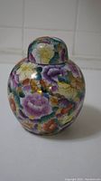 Front view of a ceramic jar with floral pattern and lid, light purple, orange, yellow flowers and green leaves.