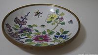 Full view of the ceramic plate showing the colorful floral pattern inside and bronze rim