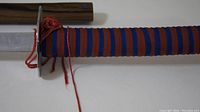Close-up of the sword handle showing blue and red cord wrap and circular metal guard (tsuba).