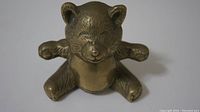 Front view showing the smiling face and sitting position with outstretched limbs of the small bronze bear figurine.