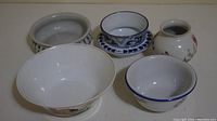 Six miscellaneous ceramic pieces including bowls, vases, and cup with saucer in various decorative styles and colors, placed on a white surface.
