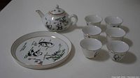 Full tea set including one teapot, six small tea cups, and a plate, all decorated with panda illustrations and gold trim