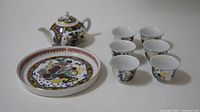 Tea set components arranged showing teapot, tray, and six cups in detail from a frontal angle.