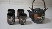 Tea set from angled top view showing four cups and teapot with woven handle