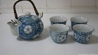 Full view of the tea set showing one teapot and four matching cups with blue floral design