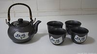 Full view of ceramic teapot and four small matching cups with floral decals on a white surface.