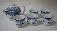 Full view of the tea set showing the teapot and five matching cups with blue floral pattern on white porcelain.