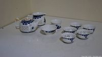 Photo showing the blue and white porcelain tea set including teapot, creamer, and seven teacups on a white surface.