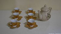 Full view of the set showing one teapot and six cups with gold patterned saucers and cup holders.