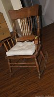 Full view of wooden rocking chair showing carved top backrest, spindle back and arms, cushioned seat, and rockers.