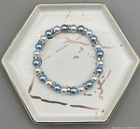 Top-down view of the bracelet laid flat on a hexagonal ceramic dish with gold and beige brushstroke detailing.