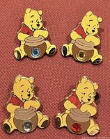 Front view of four Disney Winnie The Pooh enamel pins each showing Pooh with a honey pot decorated with a colored rhinestone: blue, yellow, clear, and red.