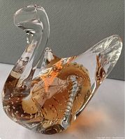 Close-up image of a single hand blown glass swan showing clear glass with orange tint and air bubbles inside.