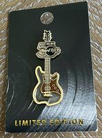 Photo of the limited edition Hard Rock collector pin in the shape of a stained glass style electric guitar on a black backing card with gold Limited Edition text.
