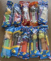 Top view of 10 new vintage PEZ dispensers in sealed original wrappers arranged in two rows on wooden floor, showing colorful character heads including Shrek and Darth Vader