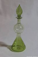 Full view of green glass perfume bottle with rounded middle section and pointed stopper.