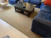 Rug positioned under dark coffee table with navy seating surrounding it. Shows full view of rug's color and pattern.