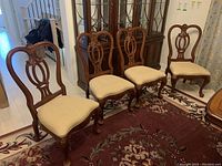 Four chairs arranged in a row showing front view of carved backs and upholstered seats.