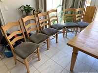 Six wood frame kitchen chairs with gray upholstered seats shown from side and front angles. Chairs are lined up next to a dining table on a tiled floor.