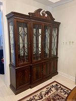 Front angle view showing entire china cabinet with hutch and buffet sections, wood finish, glass door mullions and carved top pediment