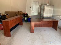 Photo showing both the wooden office desk and the hutch cabinet placed separately on a garage floor with background items including a refrigerator and boxes.