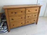 Front view of wooden dresser showing six drawers and round wooden knobs, natural wood finish, some scratches and wear visible on surface and drawers.