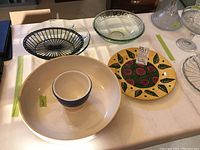 Various plates and bowls on a table including ceramic chip and dip set, glass platter and bowl, decorative ceramic plate, and metal plate.