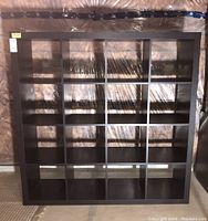 Front view of the 16 cube storage shelf unit showing 4 rows and 4 columns of square compartments against a basement wall, wrapped partially in plastic.