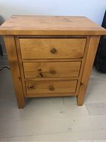 Front view of wooden side table showing three drawers with round wooden knobs, natural wood grain visible.