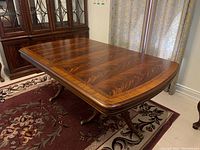 Three-quarter view of extended table showing two pedestal stands with claw feet and wood grain finish