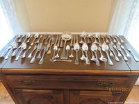 Full layout of the antique silver plated flatware laid out on a table showing multiple types and sizes of spoons, forks, knives and ladle