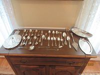 Full table view showing the collection of silver plated flatware, serving utensils, trays, and hot plate.