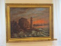 Framed oil painting showing lighthouse with rocky cliffs and stormy sea, sunset background.