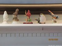 Five bird figurines displayed in a row on a white mantel showing varied bird species and colors.