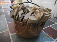 Copper chaudron filled with split firewood, showing hammered copper texture and wrought iron ring handles.