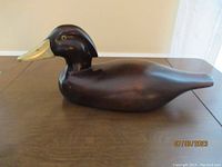 Wooden duck bird figurine with smooth dark finish and brass-colored beak, side view